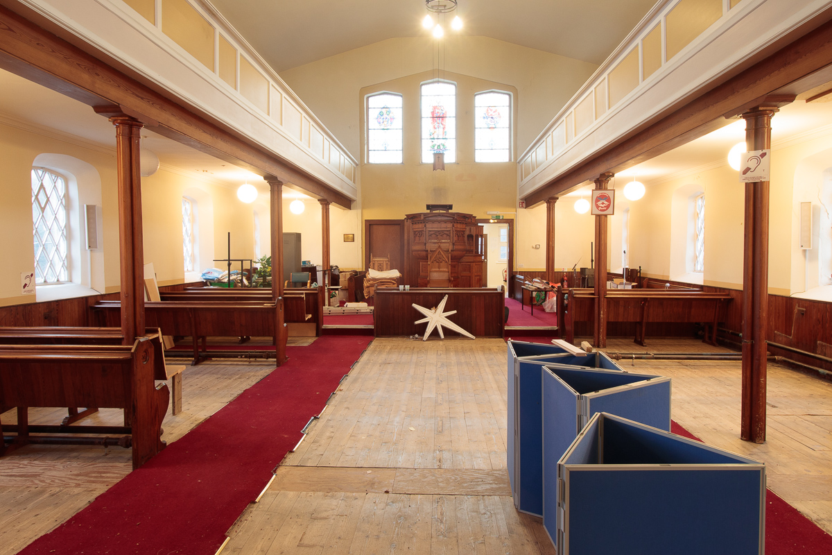 Inside of church looking to the pulpit with most of pews removed.
